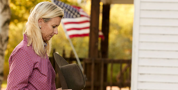 Sherry Cervi with her hat off and praying next to an American flag.